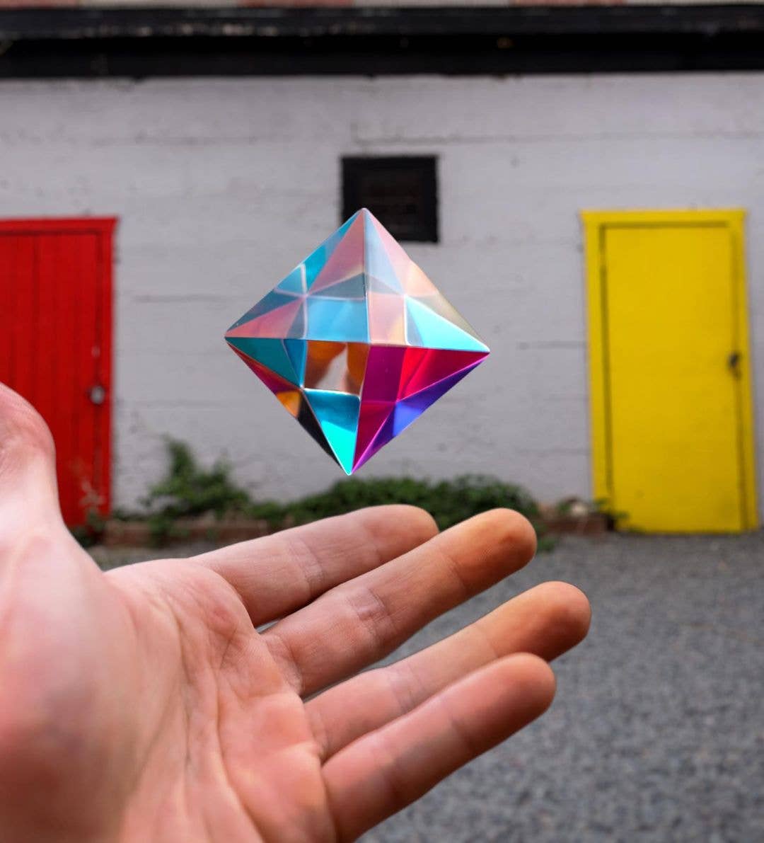Colorful geometric crystal held in front of a white wall with red and yellow doors.