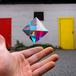 Colorful geometric crystal held in front of a white wall with red and yellow doors.