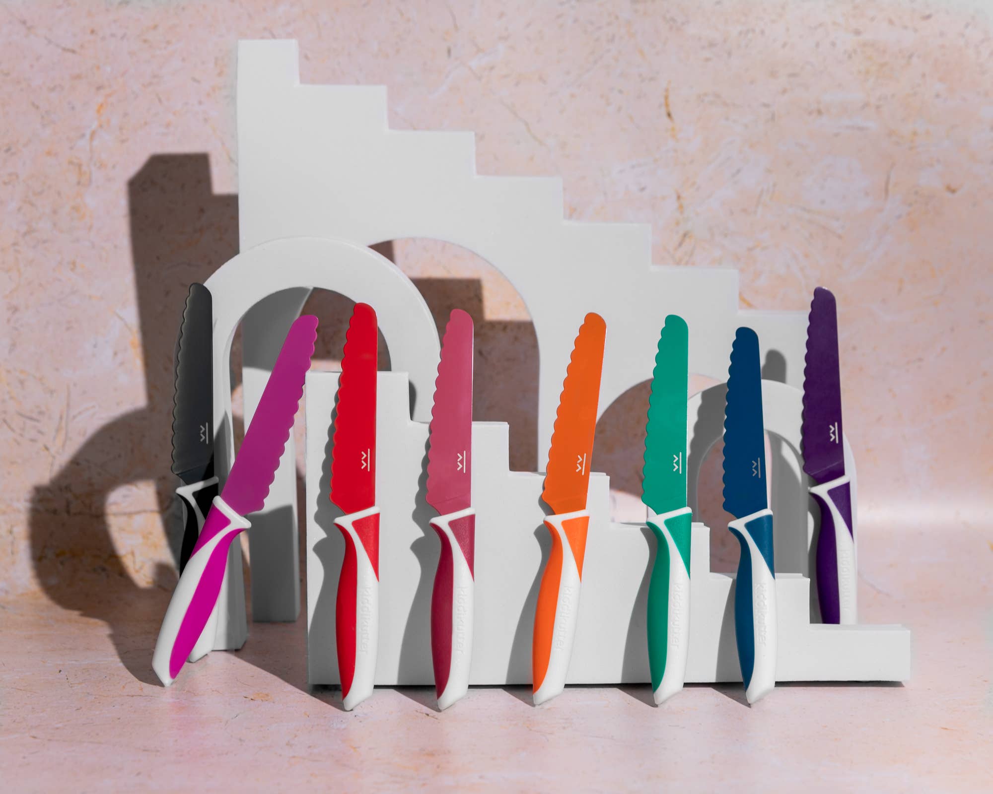 Colorful knives in a white stand on a light pink background