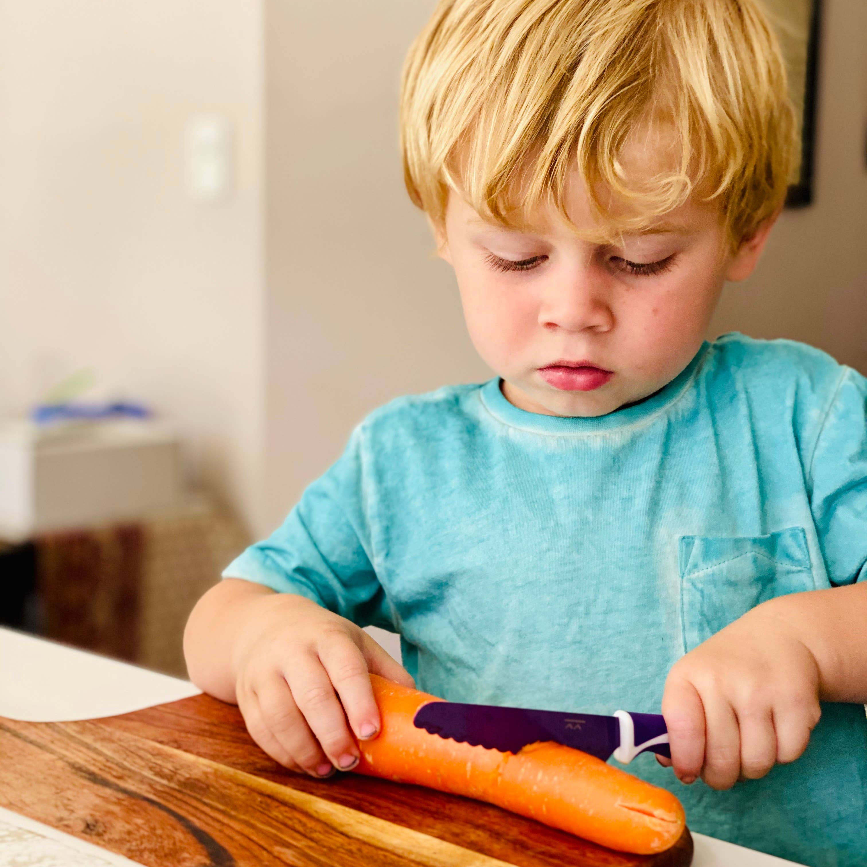 Child using a knife to cut a carrot on a wooden cutting board