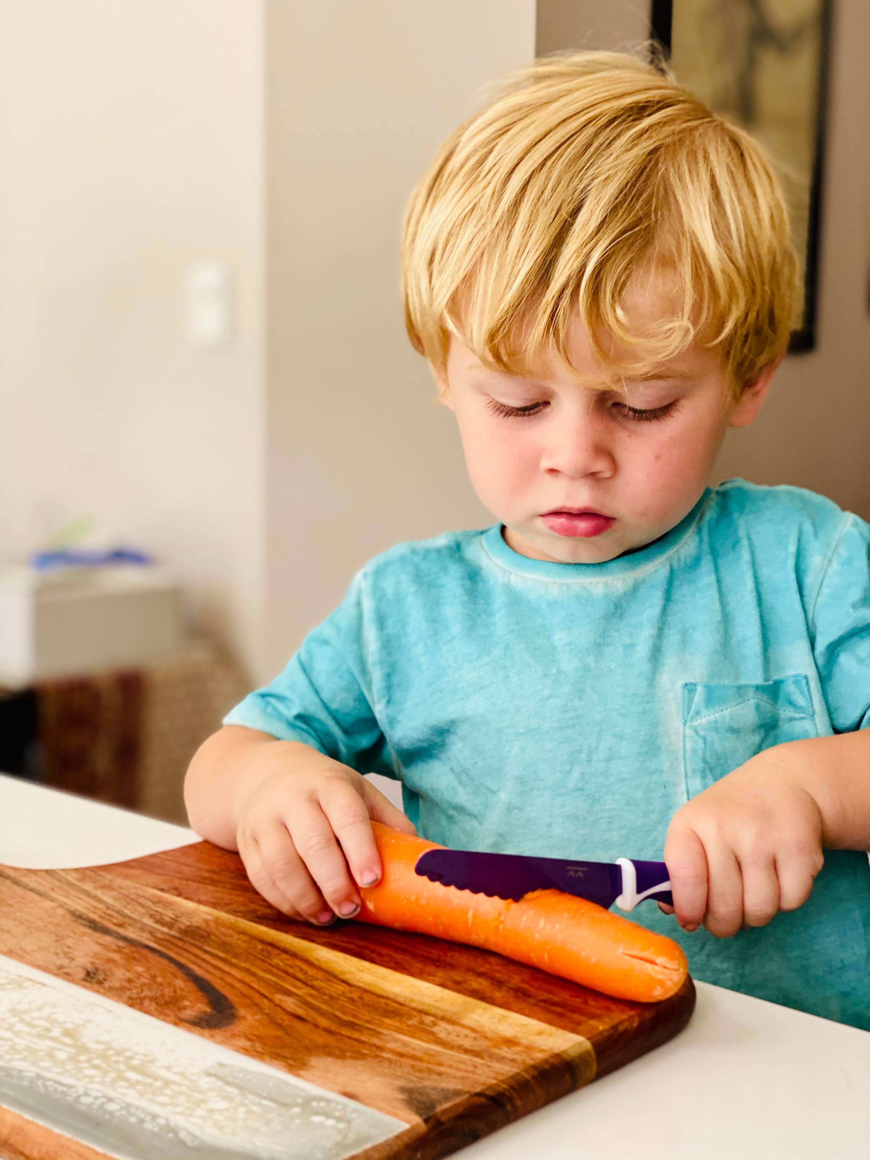 Child using a knife to cut a carrot on a wooden cutting board