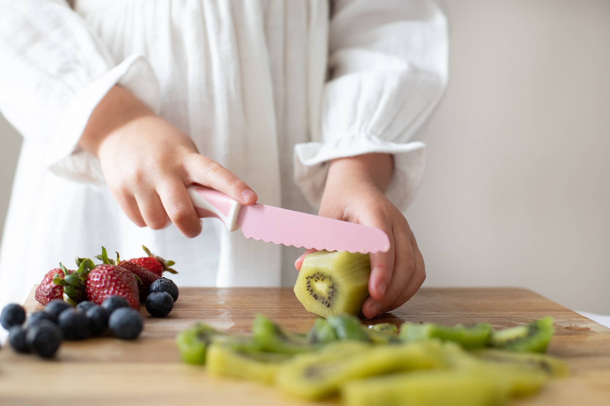 Person cutting kiwi on a wooden board with fruits in the background