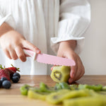 Person cutting kiwi on a wooden board with fruits in the background