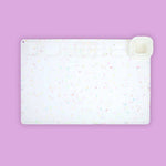 White cutting board with colorful speckles on a purple background