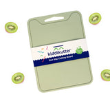 A light green kiddikutter non-stick cutting board with a white and navy paper label, shown on a white background with floating sliced kiwi fruit illustrations around it.