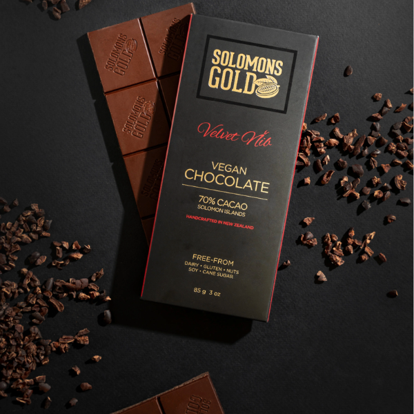 Solomons Gold Vegan Chocolate Velvet Nibs bar on a dark background with cacao nibs.