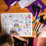 Child coloring on a magic-themed coloring book with markers and a purple drawstring bag on a wooden table.
