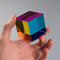 Hand holding a colorful transparent cube against a gray background