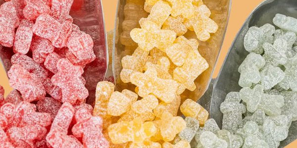 Three metal scoops filled with red, yellow, and green gummy bears on a gradient background.