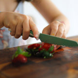 Child's hands using a kiddikutter knife to cut strawberries on a wooden cutting board.